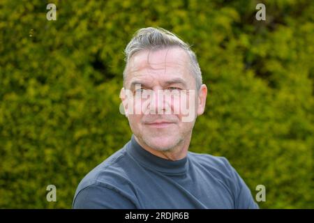 Porträt eines Mannes mittleren Alters mit grauen Haaren, der im Garten steht und seitlich neutral aussieht Stockfoto