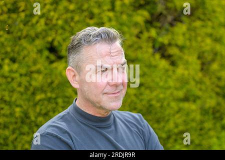 Porträt eines Mannes mittleren Alters mit grauen Haaren, der im Garten steht und zur Seite blickt Stockfoto