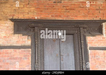 Alte geschlossene und verschlossene Holztür an einer Ziegelwand mit detaillierten Schnitzereien um die Tür herum, die den klassischen Look verleihen. Stockfoto