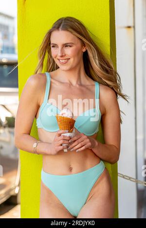 Ein wunderschönes braunes Bikinimodel genießt eine Eiskrem-Konserve, während es sich im Frühlingswetter entspannt Stockfoto