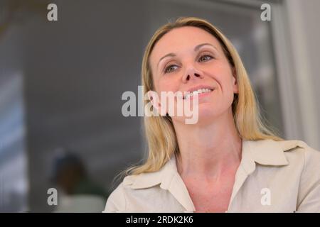 Porträt einer 40-jährigen attraktiven Frau, die auf der Terrasse sitzt und mit einem freundlichen Lächeln aufblickt Stockfoto