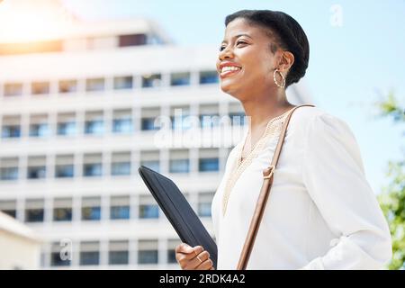 Glücklich, lächelnd und Geschäftsfrau, die mit einem digitalen Tablet durch die Stadt zu ihrem Bürogebäude geht. Selbstvertrauen, Glück und afrikanische Anwältin Stockfoto