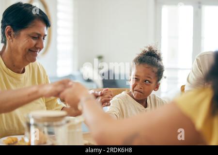 Familienhaus, Mittagessen und Händchenhalten für gemeinsame Gebete, Religion oder Glauben mit einem Comicmädchen am Tisch. Großmutter, das Kind, für das man betet Stockfoto