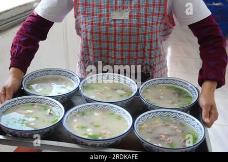 ZAOZHUANG, CHINA - 22. JULI 2023 - Ein Kellner serviert Hammelsuppe in einem Restaurant für Lammsuppen in Xiji, Shanting, Zaozhuang, Ostchina Stockfoto