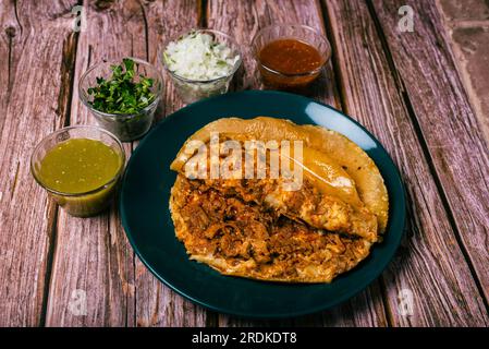 Gringa, typisch mexikanisches Gericht. Gringa Pastor a la diabla serviert mit Saucen und anderen Gewürzen auf einem Holztisch. Stockfoto