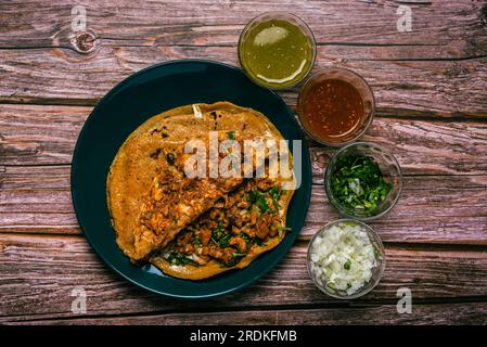 Gringa, typisch mexikanisches Gericht. Gringa Pastor a la diabla serviert mit Saucen und anderen Gewürzen auf einem Holztisch. Stockfoto