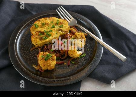 Blumenkohlsteaks gebacken mit scharfem Öl und roten Zwiebeln auf einer schwarzen Platte und Serviette, vegetarisches Gemüsegericht, Kopierbereich, ausgewählter Fokus, enge Abteilung Stockfoto