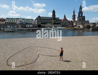 Dresden, Deutschland. 22. Juli 2023. Eine Stahlkette in Form eines Herzens liegt auf dem ausgetrockneten Elbufer gegenüber der Altstadt mit dem Ständehaus (l-r), dem Georgentor, dem Hausmannsturm und der Hofkirche, während die Dampfschiffe „Stadt Wehlen“ und „Dresden“ an der terrassenförmig angelegten Uferterrasse anlegen (Foto von der Drohne). Kredit: Robert Michael/dpa/Alamy Live News Stockfoto