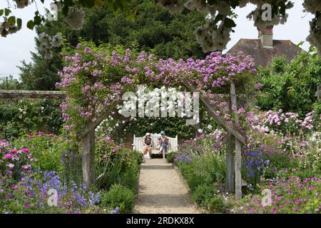 Zwei Damen auf der weißen Ltyens Gartenbank durch Kletterrosen Adelaide D'Orleans und Veilchenblau im Mottisfony Abbey Garden UK June Stockfoto