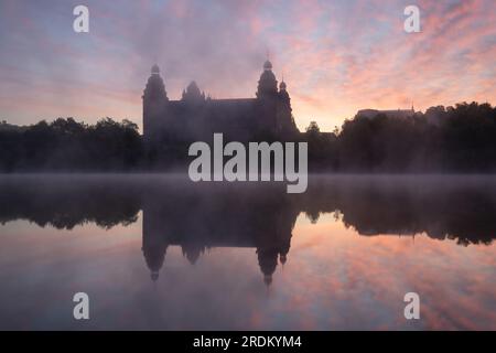 Majestätischer Sonnenaufgang: Schloss Johannisburg in Aschaffenburg, Main River. Ein atemberaubendes Spektakel, wenn die Morgensonne durch den ätherischen Nebel dringt Stockfoto