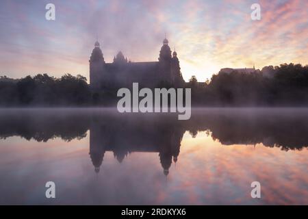 Majestätischer Sonnenaufgang: Schloss Johannisburg in Aschaffenburg, Main River. Ein atemberaubendes Spektakel, wenn die Morgensonne durch den ätherischen Nebel dringt Stockfoto