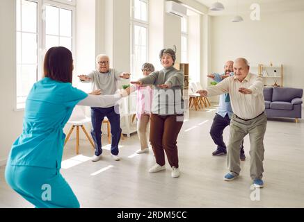 Seniorgruppe, die mit einem Physiotherapeuten im Fitnessstudio Squat macht Stockfoto