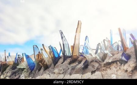 Nahaufnahme von Glasscherben an einer Wand, die zur Sicherung von Privateigentum verwendet werden, selektiver Fokus. Stockfoto