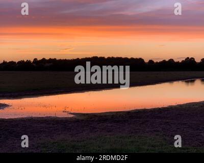 Dorney, Buckinghamshire, Großbritannien. 9. Juli 2023. Die Sonne geht über einem neuen Flutwassersee auf Dorney Common unter. Das Wasser der Themse darf überschüssiges Regenwasser in den nahe gelegenen Roundmoor Graben ableiten, und die Einheimischen, die im Dorf Eton Wick leben, mit Grundstücken, die zurück auf den Roundmoor Graben zurückgehen, klagen über den Gestank von Abwasser aus dem Wasser. Kredit: Maureen McLean/Alamy Stockfoto