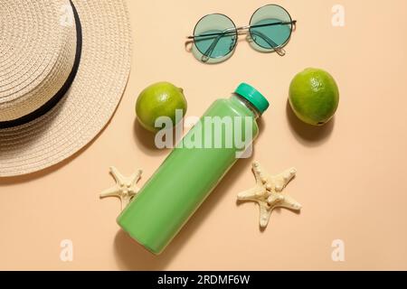 Flasche Limonade mit Strandzubehör und Limette auf beigefarbenem Hintergrund Stockfoto