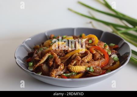 Babymais kalt. Ein chinesisches Indo-Gericht mit knackig gebratenem Babymais in einer scharfen Sauce mit sautierten Zwiebeln und Paprika. Aufnahme auf weißem Hintergrund Stockfoto