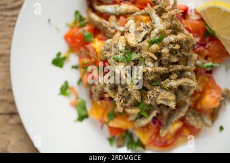 Frische Sprotten, Sprattus sprattus, die mit Mehl und Paprika überzogen wurden, bevor sie in Öl frittiert wurden. Sie werden mit einer gekochten Salsa serviert Stockfoto