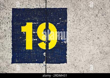 Nummer 19, neunzehn, gelbe und blaue Schablone auf grauem Hintergrund. Stockfoto