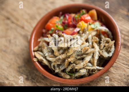 Frische Sprotten, Sprattus sprattus, die mit Mehl und Paprika überzogen wurden, bevor sie in Öl frittiert wurden. Sie werden mit einer gekochten Salsa serviert Stockfoto