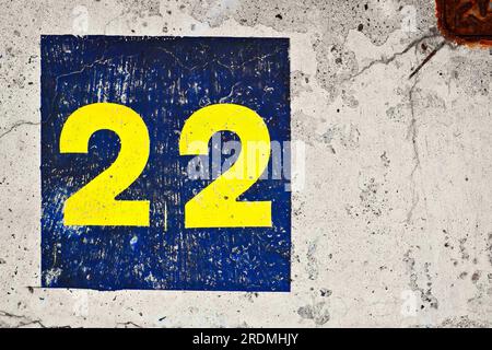 Nummer 22, 22, gelb und blau gestrichen auf grauer Betonoberfläche. Stockfoto