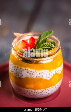 Nahaufnahme eines gesunden Desserts in einem Glasgefäß mit Mango, Chiasamen und zarter Sahne. Stockfoto