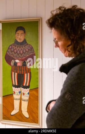 Im Juli wurden im Museum in Maniitsoq, Westgrönland, Ausstellungsstücke ausgestellt – Frau, die Gemälde mit traditioneller grönländischer Tracht anschaute Stockfoto