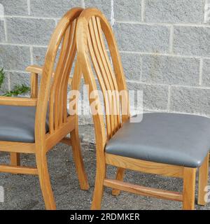 Eichensessel, einzelner heller Holzstuhl mit grauen Lederpolstern. Vorderansicht. Fotografiert vor grauem Ziegelhintergrund. Stockfoto
