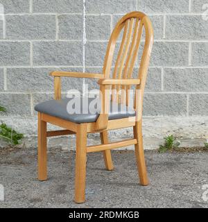 Eichensessel, einzelner heller Holzstuhl mit grauen Lederpolstern. Vorderansicht. Fotografiert vor grauem Ziegelhintergrund. Stockfoto