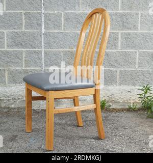 Eichensessel, einzelner heller Holzstuhl mit grauen Lederpolstern. Vorderansicht. Fotografiert vor grauem Ziegelhintergrund. Stockfoto
