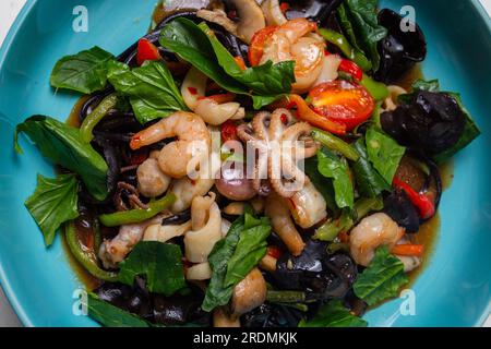 Salat aus nächster Nähe mit Meeresfrüchten und schwarzen Pilzen in einem blauen Teller von oben. Stockfoto