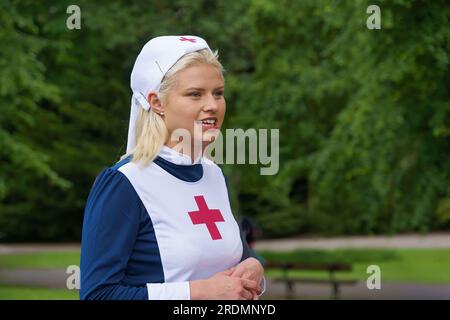 Eine junge blonde Frau in einem schicken Kleid mit 1940er Schwesternuniform mit rotem Kreuz und Mütze verkörpert charmant die Vintage-Ära auf dem Event, Valley Gardens, Stockfoto