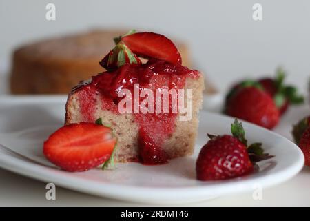 Ein Stück Erdbeerkuchen. Ein einfacher Teezeitkuchen mit frischem Erdbeerpüree. Serviert mit frisch geschnittenen Erdbeeren und Erdbeersauce. Schuss Stockfoto