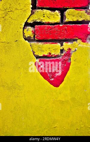 Hellgelbe Wand mit freiliegendem Mauerwerk, gesättigter gelber und roter Farbe. Stockfoto