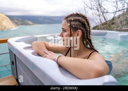 Nehmen Sie sich Zeit für sich. Badesachen im Freien mit Blick auf die Berge und das Meer. Eine Frau im schwarzen Badeanzug entspannt sich im Hotelpool und bewundert die Aussicht Stockfoto