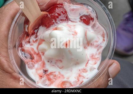 Ein köstliches Eis, serviert in einem Plastikbecher, garniert mit üppigem Obstsirup und gefüllt mit köstlichem Erdbeereis. Selektiv f Stockfoto