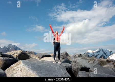 Eine Wanderin feiert, dass sie den Gipfel eines Berges erreicht, mit erhobenen Armen. Stockfoto