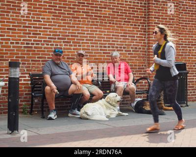 Drei ältere Männer mit Hunden, die einer jungen Frau beim Joggen vor dem Central Market in Lancaster, Pennsylvania, zuschauen, © Katharine Andriotis, 5. Juni 2023 Stockfoto