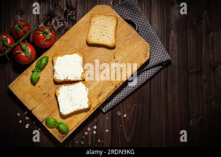 Frühstücksfoto mit Frischkäse und Brotscheiben. Tomate auf Holzhintergrund. Stockfoto