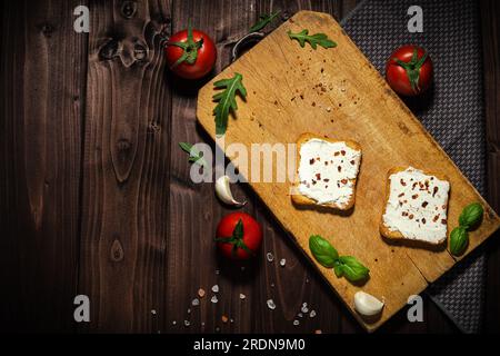 Frühstücksfoto mit Frischkäse und Brotscheiben. Tomate auf Holzhintergrund. Stockfoto
