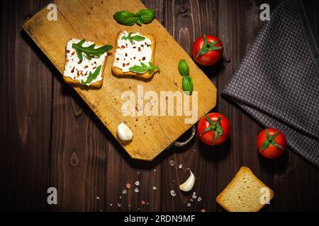 Frühstücksfoto mit Frischkäse und Brotscheiben. Tomate auf Holzhintergrund. Stockfoto