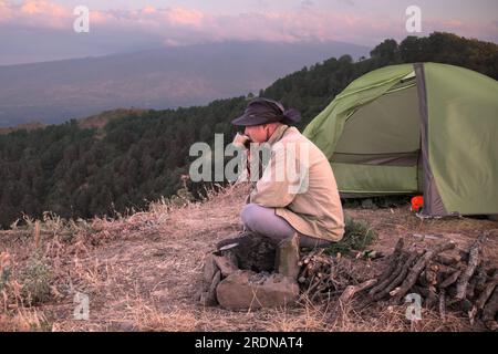 Ein Mann, der am Zelt auf dem Berggipfel des Malabotta Naturschutzgebiets in Sizilien, Italien, trinkt Stockfoto