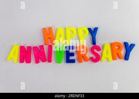 Dieses Aktienbild zeigt die Worte „Happy Anniversary“ aus farbigen Buchstabenmagneten auf einem einfachen Hintergrund Stockfoto