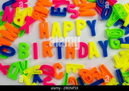 Dieses Stockbild zeigt die Worte „Happy Birthday“ aus farbigen Buchstabenmagneten auf einem einfarbigen Hintergrund. Hintergrund Stockfoto