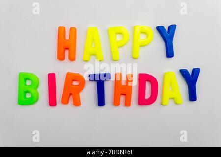Dieses Stockbild zeigt die Worte „Happy Birthday“ aus farbigen Buchstabenmagneten auf einem einfarbigen Hintergrund. Stockfoto
