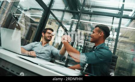 Ich freue mich, mit euch beiden jungen und gutaussehenden Männern zu arbeiten, die sich die Hand schütteln und lächeln, während sie in einem modernen Büro arbeiten Stockfoto