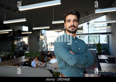 Selbstbewusster lateinischer Geschäftsmann, der im Büro steht, wegschaut und nachdenkt. Stockfoto