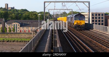 DRS-Diesellokomotive der Klasse 66 66430 an der Westküste der Hauptlinie, die einen Güterzug mit Ballastierung für Network Rail durch Lancaster transportiert Stockfoto