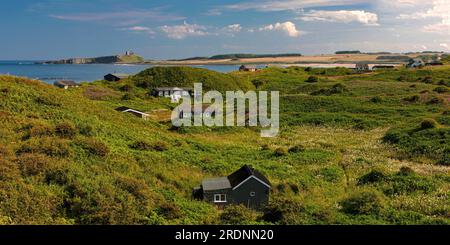 Blick in der Sommersonne in Richtung Dunstanburgh Castle an der Northumberland Coast von Low Newton mit Strand und Strandhütten im Vordergrund Stockfoto