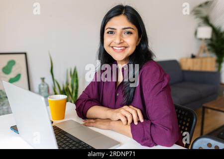 Junge inderin lächelt in die Kamera und arbeitet zu Hause mit einem Laptop Stockfoto