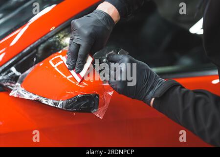 Ein Mann, der transparente Vinylfolie auf den Außenspiegel eines Autos legt, Nahaufnahme. Hochwertiges Foto Stockfoto